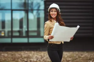 Foto de um arquiteto analisando uma planta em uma obra (ambiente externo com capacete e prancheta).
