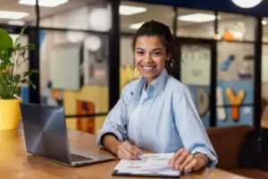 Técnica Bancária sorridente sentada na frente do seu Notebook