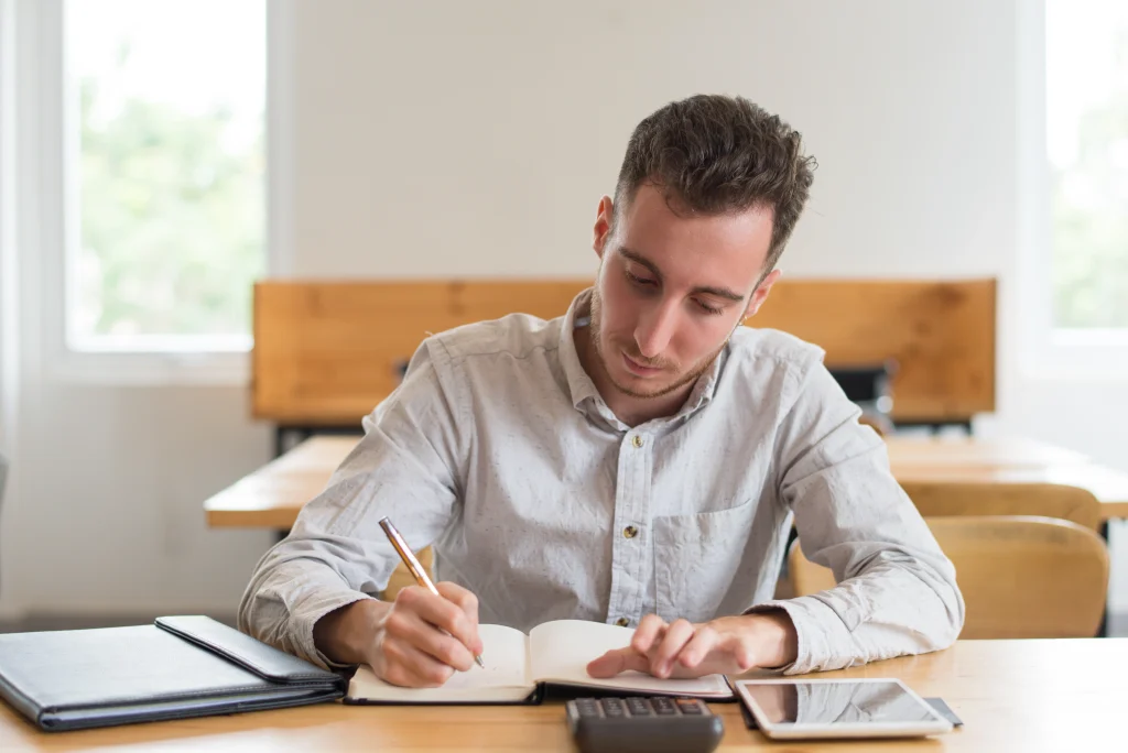 O que estudar para a prova do Detran SP? Edital publicado! 2 rapaz sentando estudando enquanto olha uma calculadora