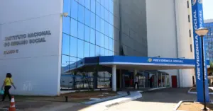 Entrada do INSS com um prédio azul espelhado atrás / Concurso INSS