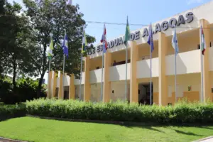 Fachada da Universidade Estadual de Alagoas (UNEAL) com bandeiras hasteadas. - Concurso UNEAL