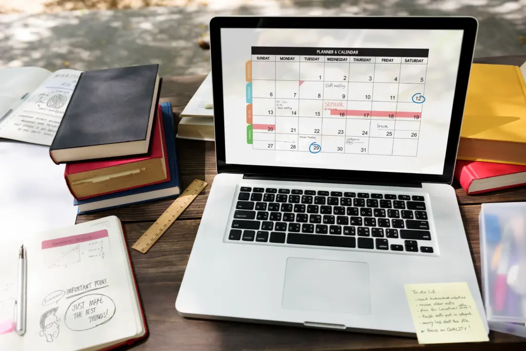 computador com agenda aberta e materiais de estudo ao lado