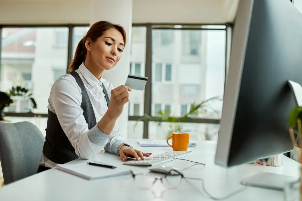 Concurso Banestes: mais de 300 aprovados foram convocados 1 Mulher em ambiente bancário segurando cartão enquanto utiliza computador, ilustrando matéria sobre o concurso Banestes convocou.